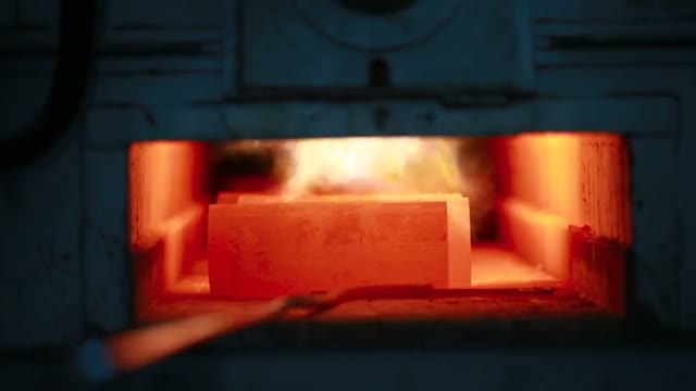 Glowing billet held by tongs at a furnace mouth