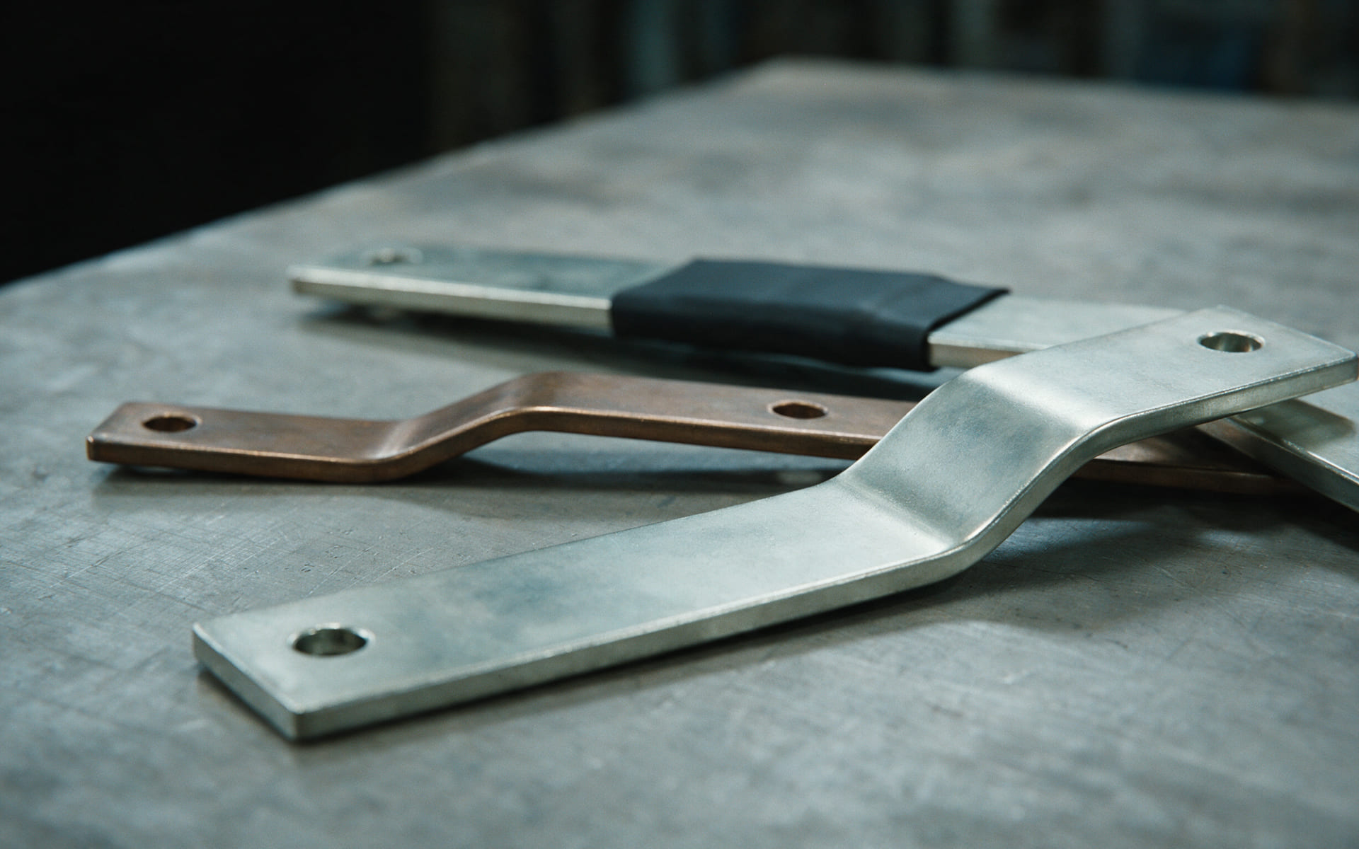 Illustration of three formed and plated busbars on a steel bench